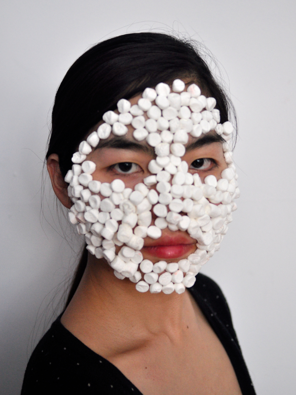 portait of a women with mini marshmallows stuck to her face. she gazes directly back at the viewer