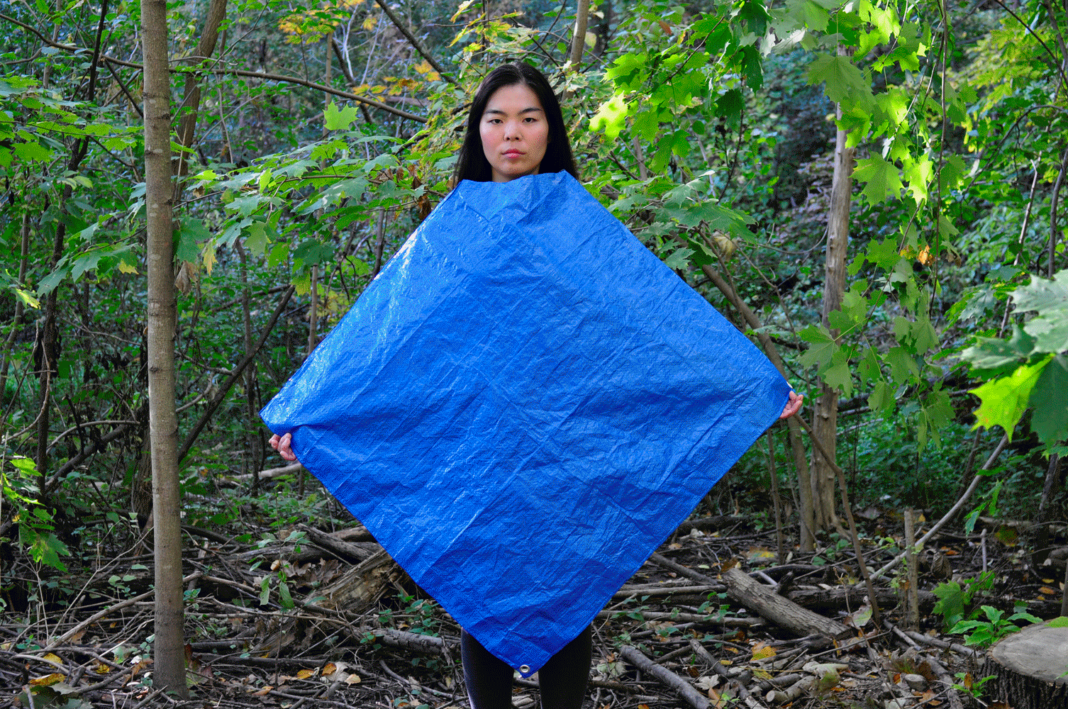 animated gif of a woman wearing a tarp as a poncho with various camping supplies stuck to the tarp