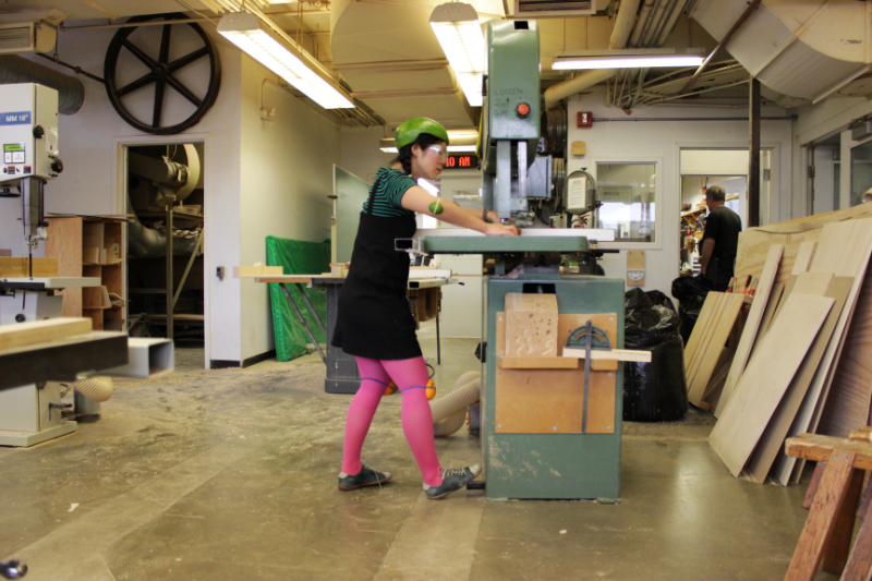 woman using a bandsaw wearing a watermelon and citrus fruit as helmet kneepads and elbowpads