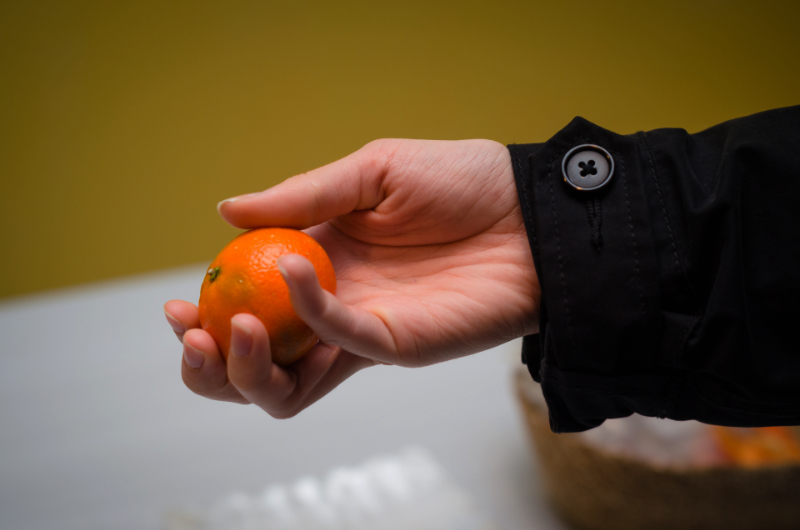 close-up of a woman's hand holding a whole tangerine